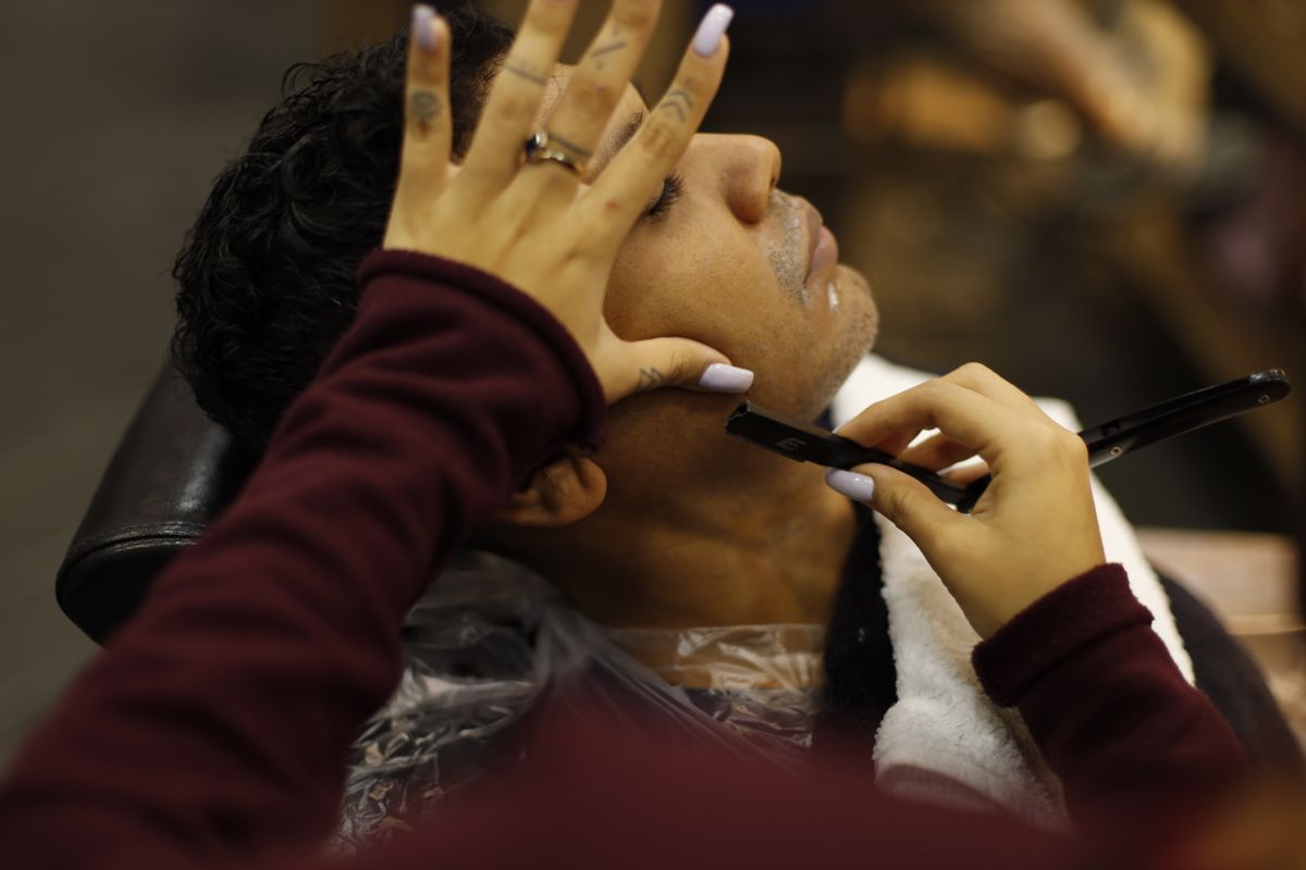 Close-up of a female barber giving a client a straight-razor beard shave